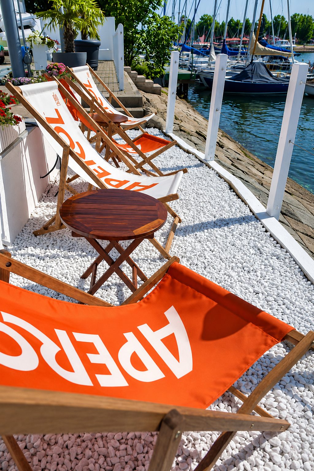 Aperol-Liegestühle auf weißem Kies am Yachthafen
